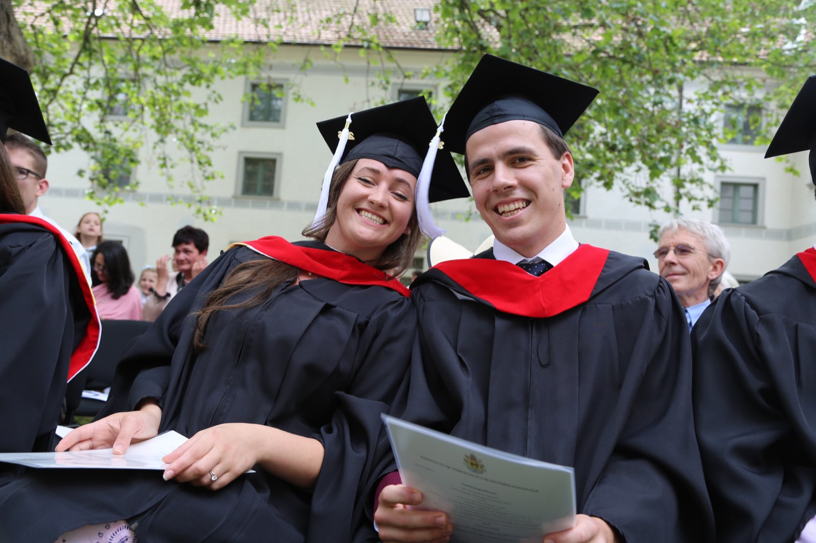 Two laughing graduates in gowns holding their diplomas