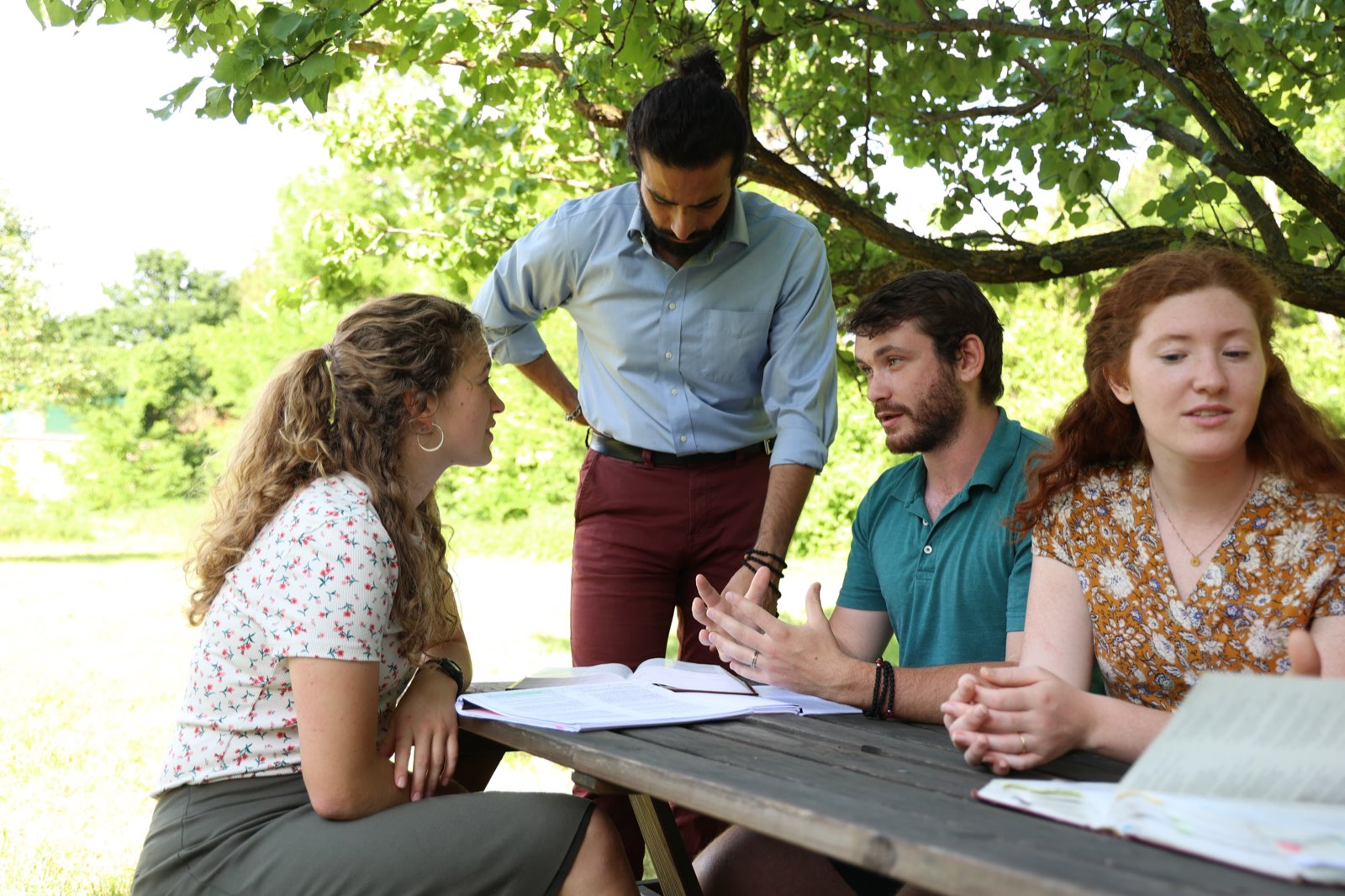 Students and a professor in lively discussion around a picnic table with open books