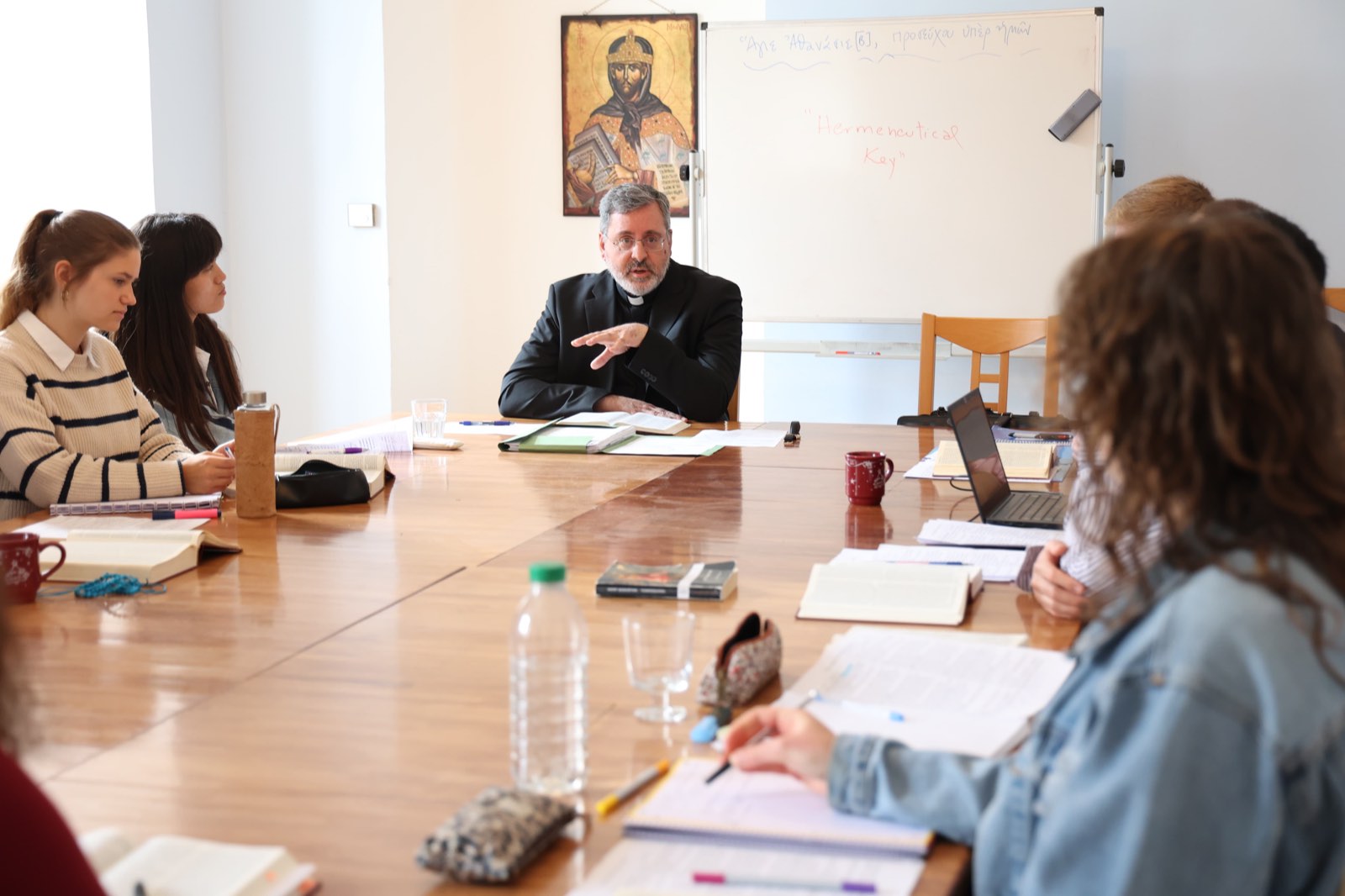 A priest-professor teaching at the seminar table beneath an icon